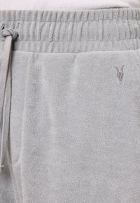 Grå sweatpants lavet af blødt, struktureret stof. Har en elastisk talje med snøre og et lille logo ved hoften.