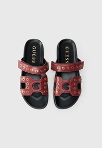 Sandales plates en cuir rouge avec accents en métal doré, design ajouré et semelles noires. Dotées de deux sangles et d'un logo bien visible.