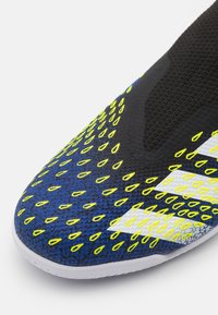 Sportovní obuv s texturovaným černoblue vrškem, který zdobí jasně žluté kapkovité vzory, bílé detaily a hladkou bílou podrážkou.