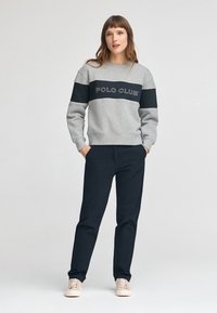 Felpa grigia con striscia nera e testo "POLO CLUB", abbinata a pantaloni scuri e scarpe chiare. Tessuto liscio e vestibilità comoda.
