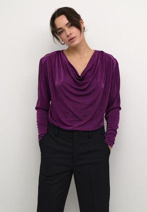 Lila långärmad topp med draperad halsringning, mjuk textur och rynkade axlar, matchad med svart byxor med hög midja.