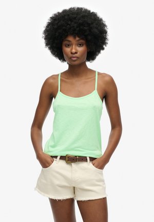 Lichtgroene katoenen tanktop met dunne bandjes, gecombineerd met beige shorts met een rafelige zoom, gedragen met een bruine riem.