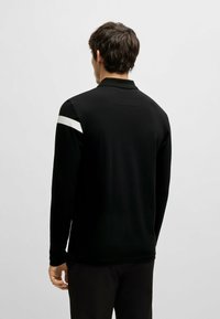 Schwarzes Langarm-Polo mit Kragen, versehen mit einem weißen Streifen über die Schulter. Hergestellt aus einem glatten, leichten Stoff.