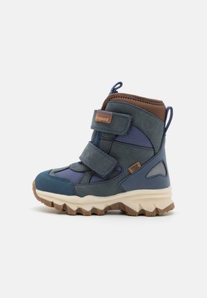 Bottes en mélange de matériaux bleu et marine avec des sangles Velcro, des accents marron et une semelle en caoutchouc texturée présentant un motif en zigzag.