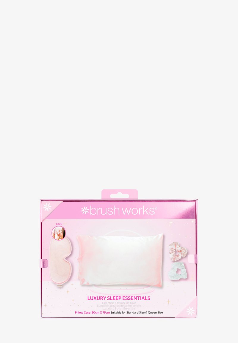 El conjunto incluye una funda de almohada rosa suave y brillante, una máscara para dormir y dos scrunchies en colores pastel. El embalaje es rosa con texto blanco.