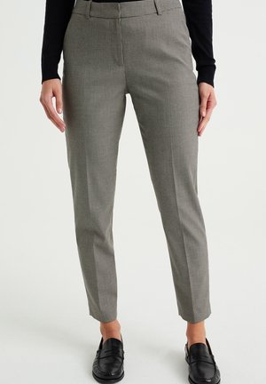 Kvinde iført sort-hvide houndstooth skinny bukser med sorte loafers og en sort langærmet top, stående mod en hvid baggrund.