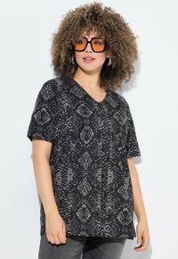 Černé a šedé tričko s výstřihem do V a vzorem hada, krátké rukávy a volný střih. Nosené s tmavými džíny a oversized slunečními brýlemi.