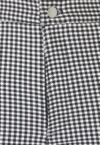Gros plan d'un tissu pied-de-poule noir et blanc avec un bouton en métal et une couture visible.