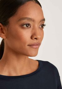 Indumento blu navy con scollatura arrotondata. Vista ravvicinata che mette in mostra la texture liscia e il tono naturale della pelle, con tratti facciali ben definiti.