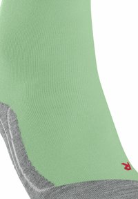 Calza verde elastica con tallone e punta grigi, caratterizzata da un logo rosso. Il materiale ha una consistenza liscia con un design a coste.