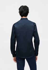Marineblauw shirt met lange mouwen, een kraag, een gladde textuur en manchetten met knopen. Heeft een rechte zoom en zijsplitten ter hoogte van de taille.