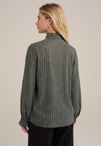 Zöld, félig áttetsző blúz függőleges csíkokkal és texturált pöttyökkel. Ráncos gallér, hosszú ujjú, gombos mandzsettával, laza fazon.
