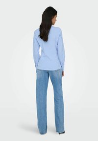 Chemise rayée bleu clair cintrée à manches longues, poignets à boutons et ourlet arrondi, associée à un jean en denim clair taille haute à jambes larges.