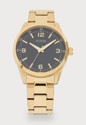 Montre dorée avec un cadran noir, grands chiffres aux positions 12, 3, 6 et 9, et un élégant bracelet à maillons. Comprend des aiguilles des heures et des minutes bien en vue.