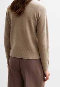 Beige Kaschmirpullover mit Rundhalsausschnitt, geripptem Saum und Bündchen. Weiche Textur, figurbetonte Silhouette, getragen mit hellbraunen Hosen.