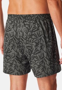 Schwarze gemusterte Badeshorts mit einem blättrigen Design, ausgestattet mit einem elastischen Bund und einer lockeren Passform. Das Material wirkt leicht und glatt.