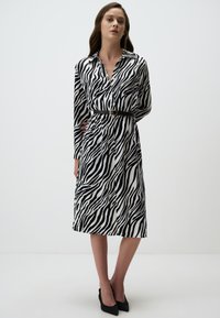 Zwart-wit gestreepte jurk met lange mouwen, kraag en een cinched taille detail met een zwarte riem. Elegante rechte snit.