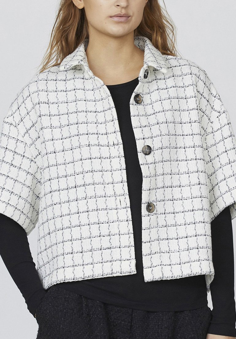 Hvid cropped jakke med sort rutenetmønster, der har en krave og tre mørke knapper. Tekstureret stof med korte ærmer.