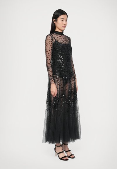 Black long-sleeve dress featuring sheer tulle fabric, embellished with sequins and a fitted bodice, paired with black heeled sandals.