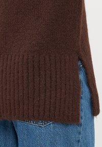 Brauner Strickpullover mit geripptem Saum und texturiertem Finish. Kombiniert mit hellblauen Jeans.