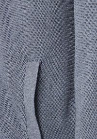 Nära bild av en texturerad grå stickad tyg med en ögla integrerad i mönstret.