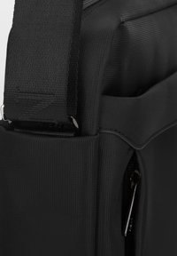 Czarna torba na laptopa z tkaniny, charakteryzująca się gładką teksturą, regulowanym paskiem i kieszenią na zamek. Kompaktowy design z elegancką sylwetką.