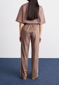 Brown cotton blend oversized t-shirt and matching trousers with elastic waistband. Pants feature side seams and a straight-leg fit.