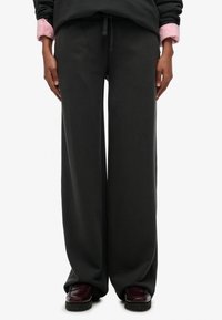 Sweatpants med vide ben i mørkegråt stof, med snøre i taljen, glat tekstur og forlommer. Båret med bordeaux farvede loafers.