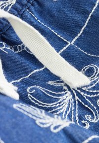 Gros plan sur un tissu bleu avec des motifs floraux brodés blancs et un cordon blanc tissé noué en un nœud.