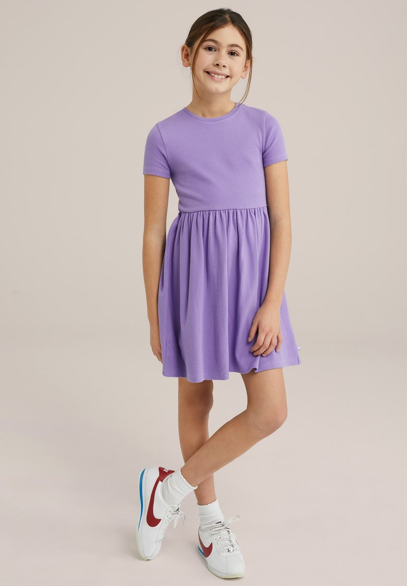 Violet trumpas rankovėmis suknelė su prigludusia apykakle ir platėjančia sijonu. Dėvima su baltais sportbačiais su raudonais akcentais ir mėlynomis padangomis.