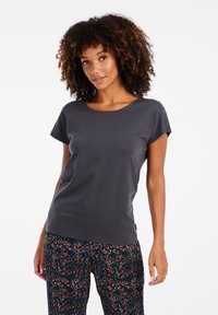 Graues kurzärmeliges T-Shirt aus weichem Material mit rundem Ausschnitt, kombiniert mit gemusterten schwarzen und bunten Schlafanzughosen.