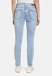 Jean skinny en denim bleu clair avec une taille mi-haute, cinq poches et des détails de couture visibles, assortis à des baskets blanches.