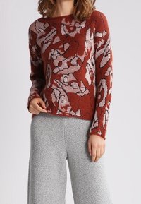 Strikket sweater i rødbrun med blomsterprint i lyse farver. Har en bred halsudskæring og lange ærmer. Kombination med grå vidde bukser.
