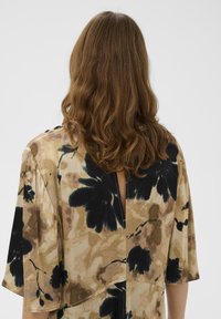 Tunică cu imprimeu floral multicolor, potrivire lejeră, mâneci scurte și deschidere la spate, cu o combinație de nuanțe bej, negru și verde subtil.