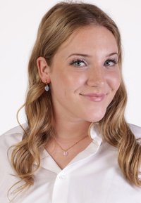 Gouden oorbellen in de vorm van hoepels met een blauwe hartvormige accent. Het model draagt een witte overhemd met knopen en een gouden ketting met een hart-hangertje.