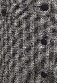 Tela de tweed en blanco y negro con un patrón de pata de gallo. Cuenta con cuatro botones negros y un pequeño bolsillo frontal. Superficie texturizada, diseño estructurado.