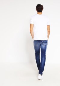 Smal passform blå denimjeans med medel tvätt, med bakfickor och en vit t-shirta med korta ärmar. Bärs med vita sneakers.