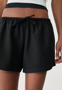 Zwarte katoenen shorts met een elastische tailleband en trekkoord. Heeft een zachte textuur en een relaxte pasvorm.