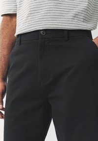 Zwarte katoenen broek met een slim fit, voorzien van een enkele knoopsluiting, zijzakken en een gladde stoftextuur.