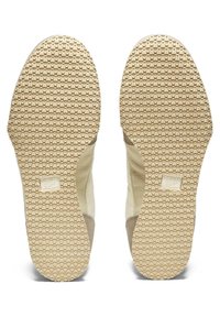 Sålene på skoene har en tekstureret gummioverflade med små hævede cirkler, lys beige farve og en tan ruskindaccent på siderne.