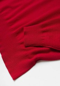 Manche et bas de pull en maille rouge avec bords-côtes aux poignets et à la taille, posé à plat sur une surface blanche.