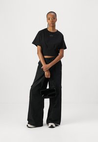 Svart kortärmad cropped t-shirt, svarta vida cargobyxor och en liten svart glänsande handväska. Texturerade sneakers fulländar looken.