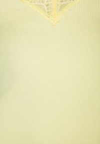 Ljusgul ribbad stickad topp med v-ringning och spetsdetaljer samt intrikata dekorationer. Mjuk textur med en figurnära silhuett.