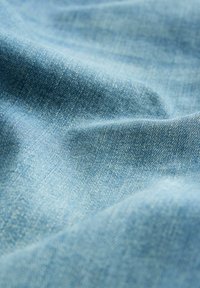 Tessuto di denim blu chiaro con una texture morbida e una trama ben visibile, caratterizzato da sottili variazioni di tono e lievi pieghe.