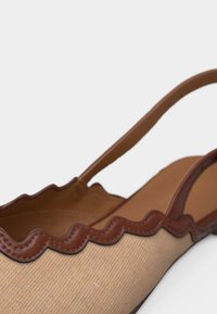 Γυναικείο μπεζ ύφασμα παπούτσι με καφέ δερμάτινη διακόσμηση με κυματιστό σχέδιο και λεπτό λουράκι στον αστράγαλο σε λευκό φόντο.