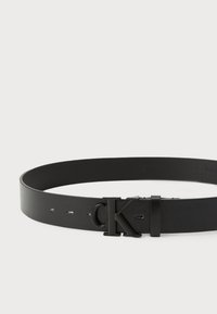 Ceinture en cuir noir à texture lisse, dotée d'une boucle en métal noir brillant avec le logo "CK". Ajustable grâce à plusieurs trous perforés.