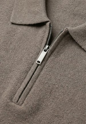 Close-up van bruin gebreide stof met een gedeeltelijk dichtgeritste zilverkleurige metalen rits en een opgevouwen kraag op een kledingstuk.