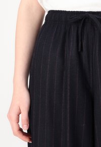 Navy striped pants with an elastic waistband and drawstring. Features fine vertical lines with a soft texture. Smooth fabric drapes loosely.