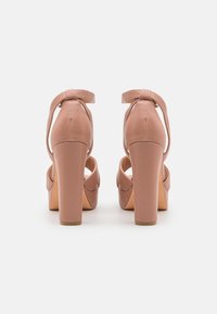 Chaussures à talons hauts roses avec une texture lisse, design à bout ouvert et bride de cheville avec une boucle. Le talon carré ajoute de la stabilité.