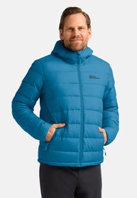 Blaue isolierte Jacke mit Kapuze, ausgestattet mit einem Reißverschluss vorne, vertikalen Steppnähten und Seitentaschen. Markenlogo auf der Brust sichtbar.